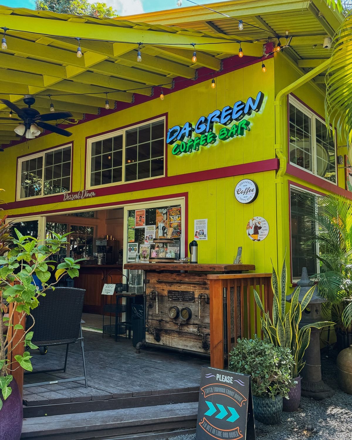 The lime-green Da Green Coffee Bar storefront with a glowing neon sign, string lights, and a rustic wood coffee counter framed by tropical plants.